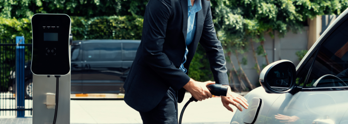 Closeup progressive black suit businessman insert EV charger plug from public charging station to his electric car. Eco friendly electric rechargeable car with zero CO2 emission.